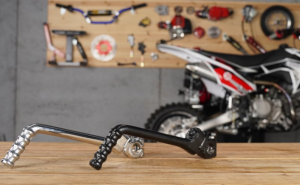 Motorcycle footpeg in foreground with serrated grip surface. Blurred background shows parts of a motorcycle and tools.