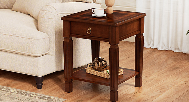 Beistelltisch aus braunem Holz mit Einzelschublade und unterer Ablage, der neben einem cremefarbenen Polstersofa im Wohnzimmer mit weißen Vorhängen positioniert ist.