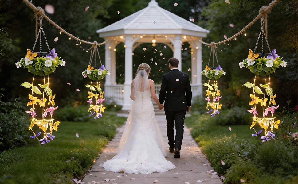 Bride and groom walking down outdoor aisle toward white gazebo with golden hanging floral decorations and green lawn, evening wedding ceremony setting.