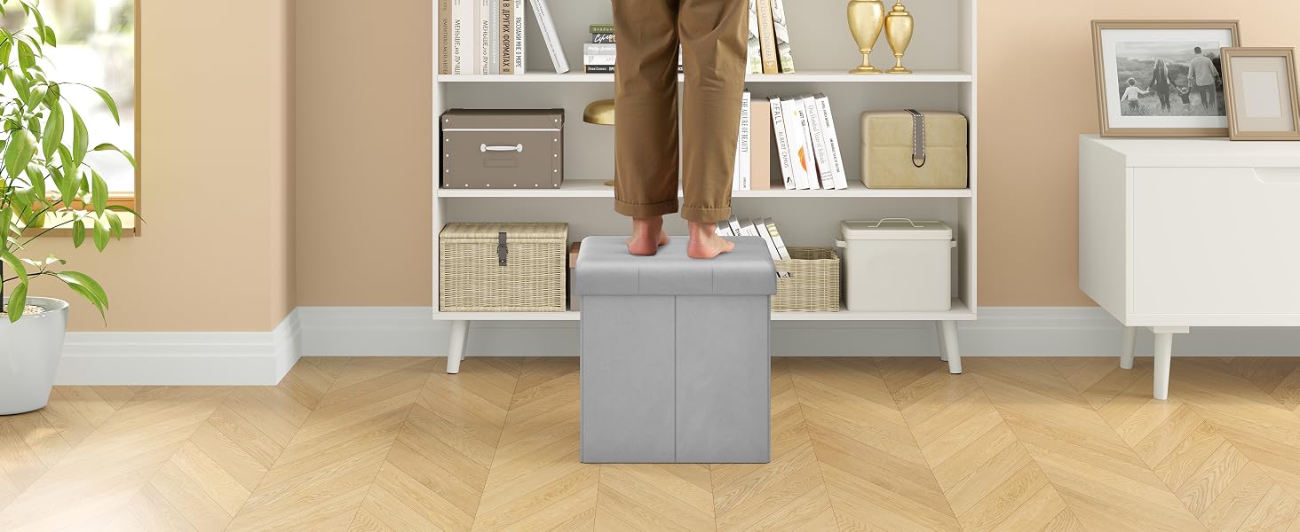 Un objeto gris con forma de cubo, posiblemente un taburete o una otomana, se encuentra sobre el suelo de madera de una sala de estar con muebles blancos