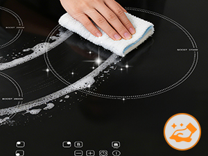 Gros plan de la surface de la table de cuisson à induction noire essuyée avec un chiffon blanc, montrant une finition noire brillante et un cercle indicateur orange dans le coin inférieur droit.