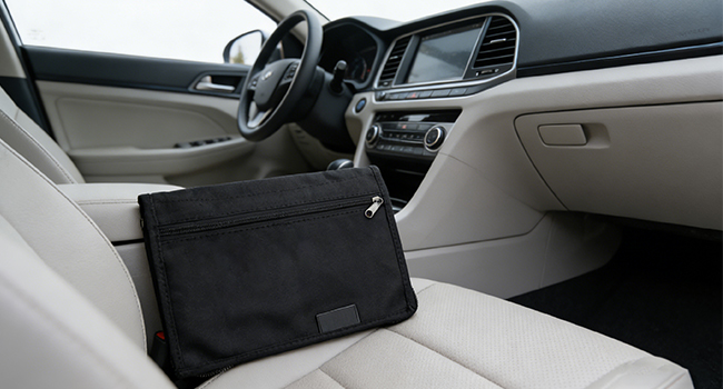 Interior view of a vehicle's front cabin, showing light-colored leather dashboard and seats, with a black bag placed on the passenger seat.