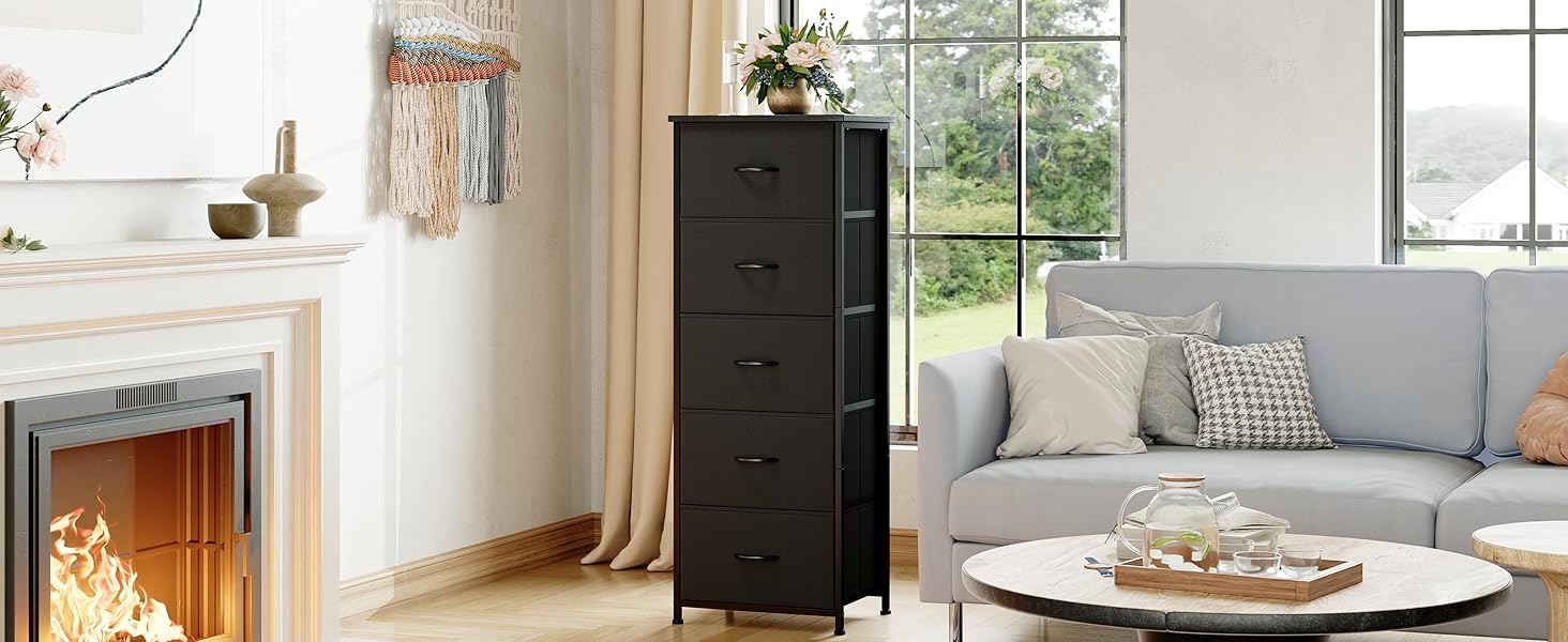 Intérieur du salon avec armoire de rangement haute noire, canapé gris, table basse ronde et cheminée. Les grandes fenêtres laissent entrer la lumière naturelle.