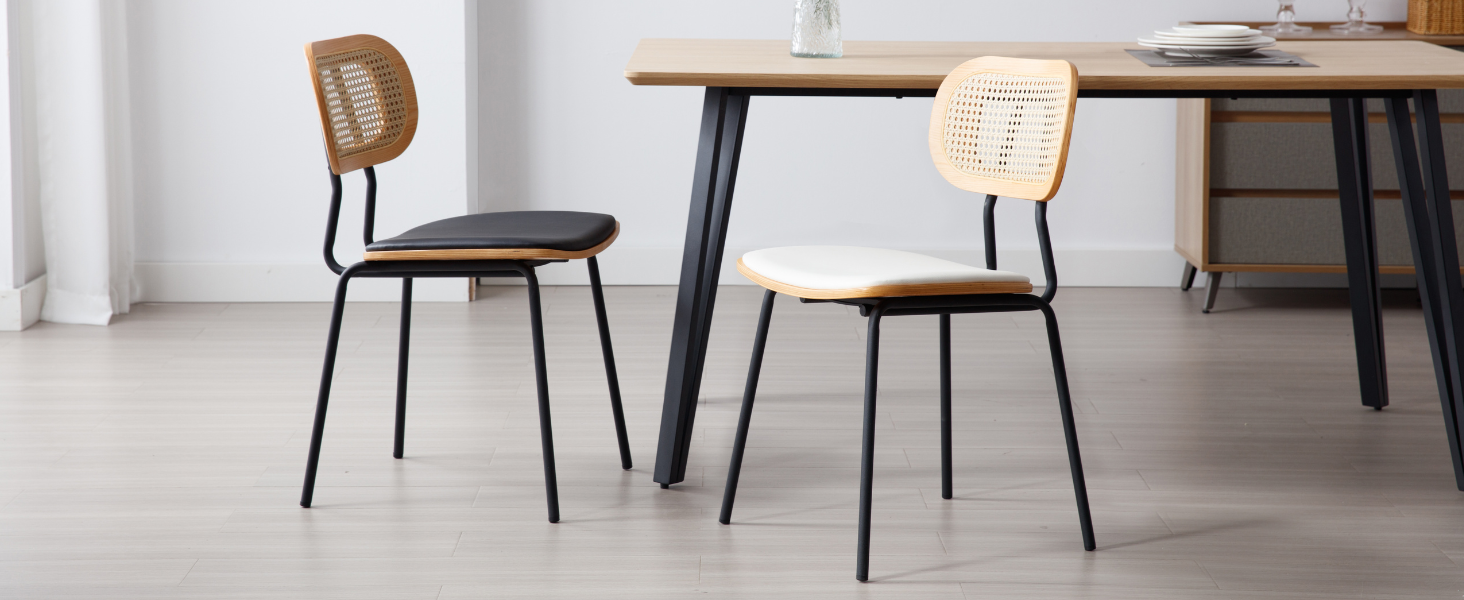 Zwei Esszimmerstühle mit schwarzem Metallgestell, gewebten Rattan-Rückenlehnen und gepolsterten Sitzen. Ein Stuhl hat einen schwarzen Sitz, der andere einen weißen, der neben einem Holztisch
