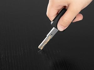 Mano que sostiene un objeto cilíndrico en forma de bolígrafo de color blanco y oscuro sobre un fondo texturizado negro.