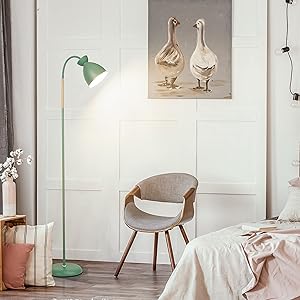 Modernes Schlafzimmer mit grüner Stehlampe, grauem Polsterstuhl und Wandkunst mit Gänsen. Weiße Wände und Holzböden sorgen für eine minimalistische Ästhetik