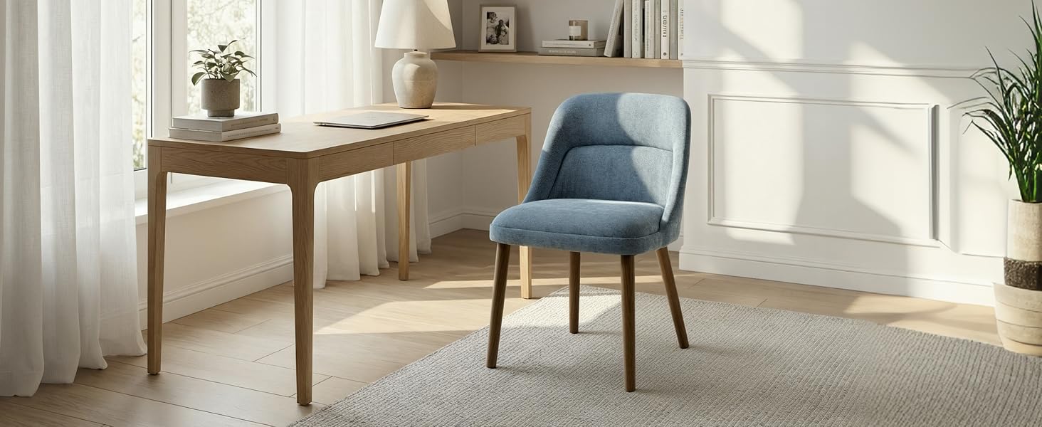 Bright, sunlit interior room setting with wooden furniture including tables and chairs, featuring large windows with sheer curtains casting natural light.