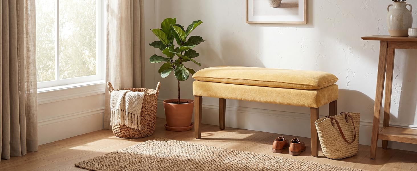 Sunlit modern living room interior featuring minimalist furniture, beige bench seating, potted plant, and natural light streaming through windows with sheer curtains.