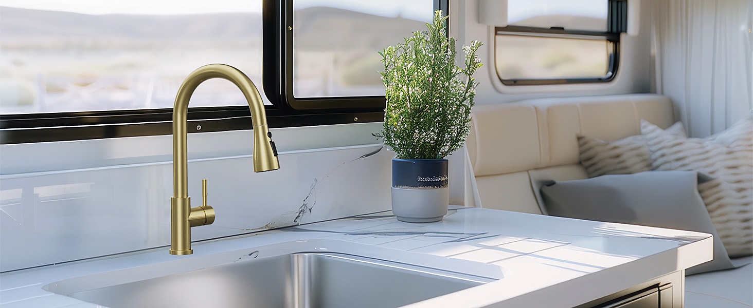 Modern kitchen sink with gold-finished pull-down faucet, white countertop, and small potted plant decoration near window.