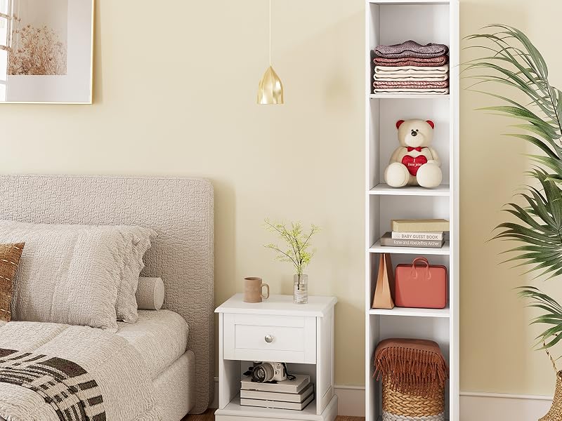 Set di mobili per camera da letto che include una libreria bianca stretta, un comodino bianco con cassetto e una vista parziale di un letto imbottito grigio. Oggetti decorativi