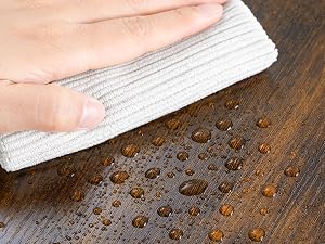 Panno bianco che rimuove le gocce d'acqua dalla superficie in legno, dimostrando resistenza ai liquidi o azione pulente.