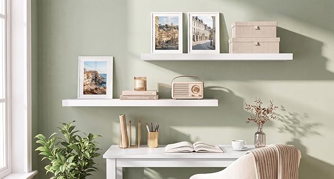 Regaldesign für Zuhause und Büro mit weißen, schwebenden Regalen mit gerahmten Kunstwerken, Aufbewahrungsboxen, Topfpflanzen, Schreibtischzubehör aus Holz und Dekorationsgegenständen an einer salbeigrünen Wand.