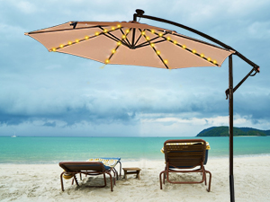 Beige cantilever beach umbrella shading two empty lounge chairs on a pristine beach with turquoise water and blue sky.
