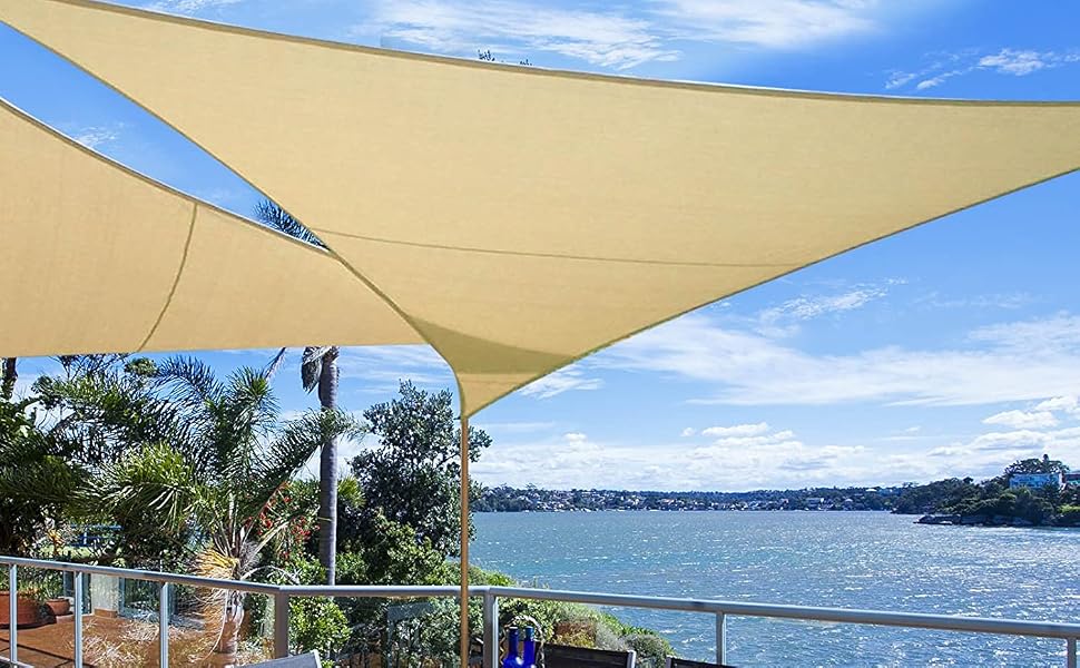 Patio esterno con tavolo e sedie sotto un grande parasole triangolare, con vista sul lungomare con palme e litorale in lontananza