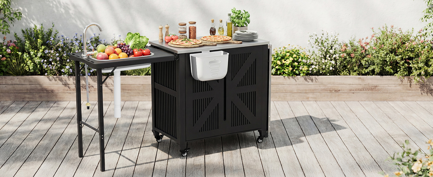 Schwarzer Outdoor-Küchenwagen mit Edelstahloberfläche auf einer Holzterrasse. Verfügt über Staufächer, eine Seitenablage mit Obst und Gemüse und ein weißes Handtuch, das am Griff hängt.