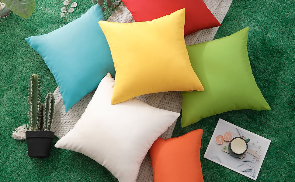 Collection de coussins décoratifs de différentes couleurs, dont le turquoise, le jaune, le vert et le blanc, disposés sur un fond texturé vert.