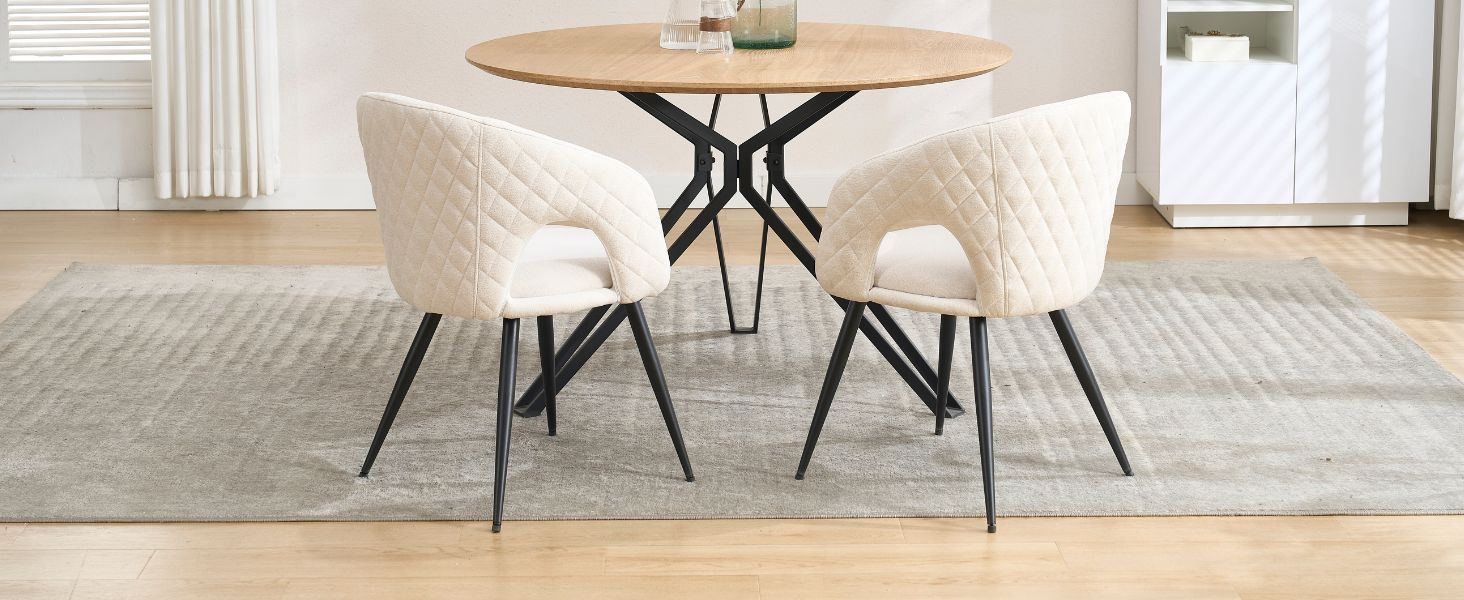 Ensemble de salle à manger moderne comprenant une table ronde en bois avec base en métal noir, associée à deux chaises rembourrées crème matelassées sur des pieds en métal noir.