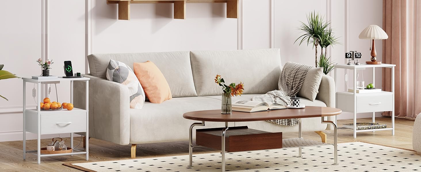 Intérieur de salon moderne avec canapé gris clair, tables d'appoint blanches, coussins décoratifs et plantes. Dispose d'un tapis à motifs géométriques et d'une décoration minimaliste.