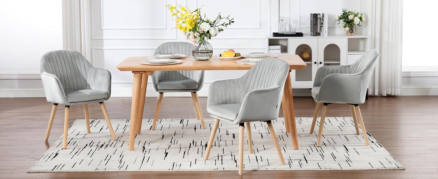 Modern dining set with wooden table, gray upholstered chairs, geometric patterned rug, and decorative floral arrangements.