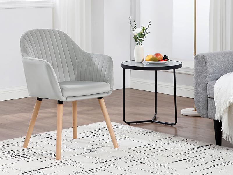 Light gray upholstered armchair with wooden legs next to small round black side table. Partial view of sofa and decor in background.