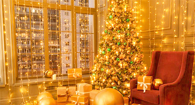 Chambre à lumière chaude avec sapin de Noël décoré, guirlandes lumineuses, fauteuil rouge et fenêtre avec vue sur la ville, créant une ambiance de vacances chaleureuse