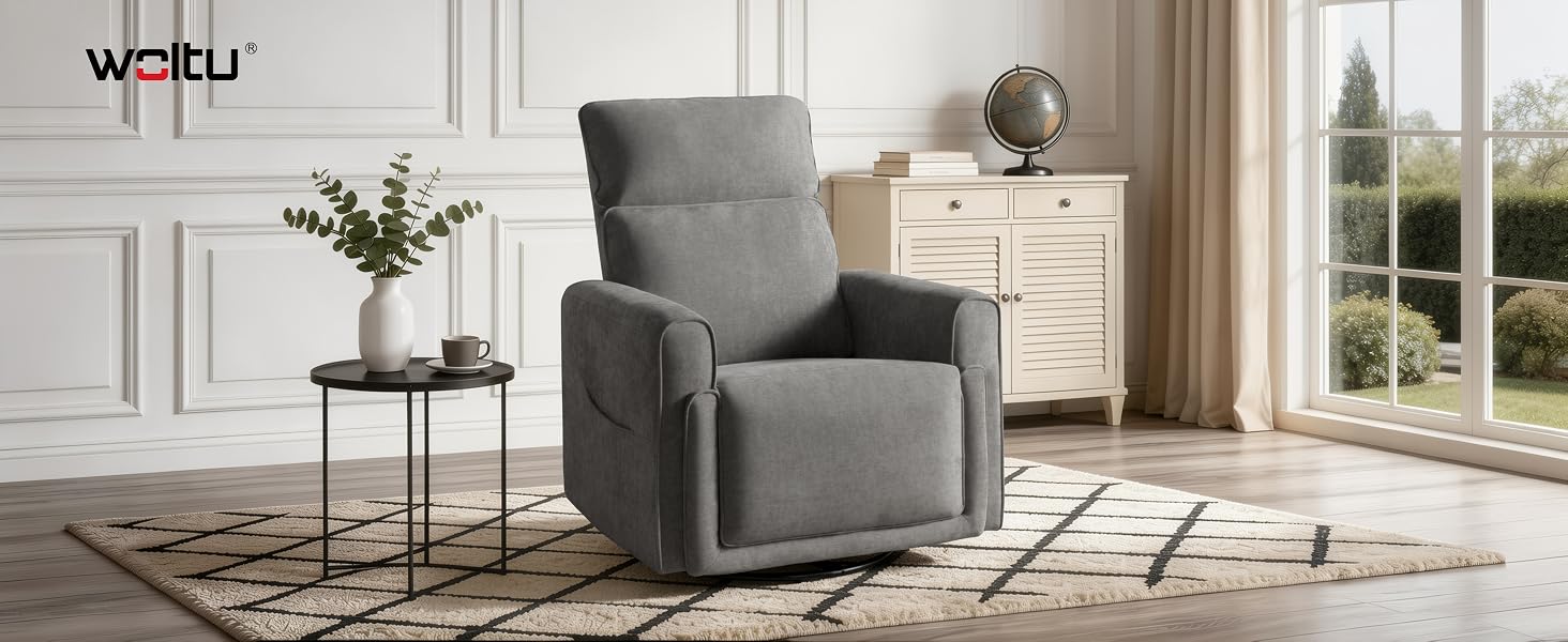 Sillón tapizado gris con patas de madera colocado en una sala de estar moderna con paredes blancas, plantas y mesa auxiliar visibles.