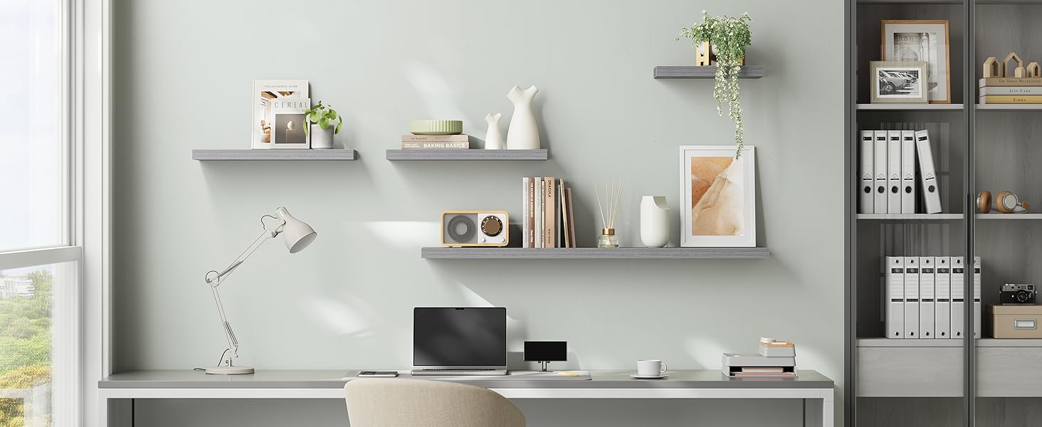 Moderna configurazione per l'home office con mensole a parete galleggianti che espongono libri, oggetti decorativi e apparecchiature tecnologiche contro una parete grigio chiaro.