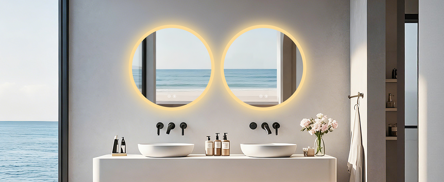 Moderno bagno interno con due specchi ovali retroilluminati sopra il lavabo bianco galleggiante. Vista sull'oceano visibile attraverso le finestre, arredamento minimale con piccoli vasi.