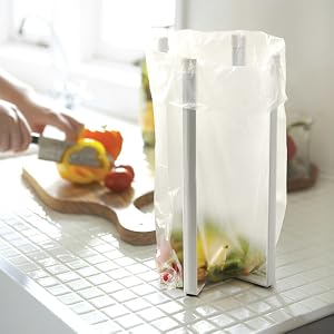 Le texte se lit comme suit : « Image 3 ». Porte-sac ou distributeur en plastique transparent monté sur une surface blanche, illustré en cours d'utilisation avec les fruits et légumes et la planche à découper visibles.