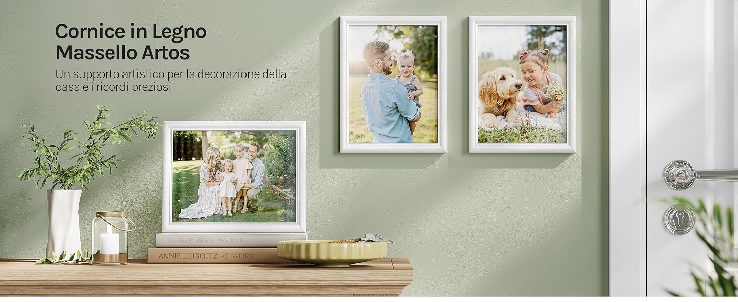 Il testo recita «Comice in Legno Massello Artiza» con il testo dei sottotitoli in basso. Espositore da parete interno con stampe di opere d'arte botaniche incorniciate su una parete verde salvia sopra una mensola in legno con vaso bianco e oggetti decorativi.