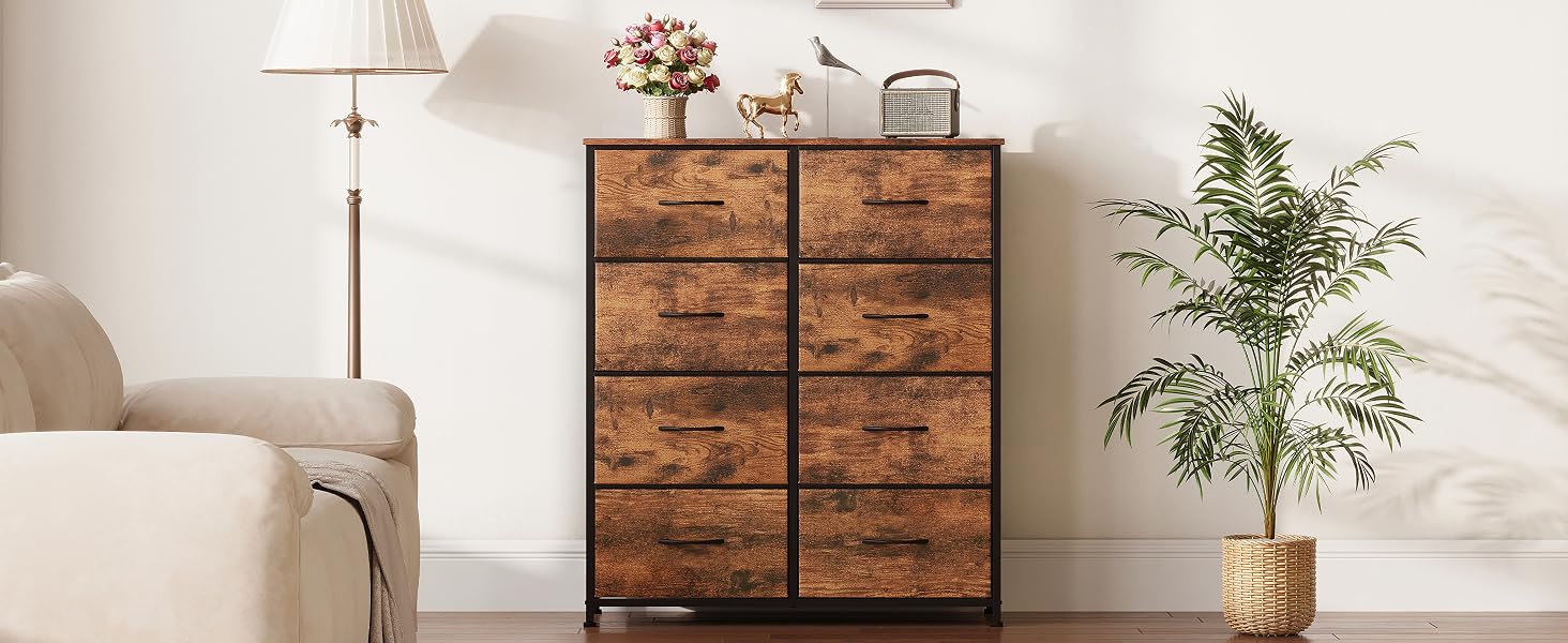 Commode rustique en bois avec six tiroirs, structure en métal foncé. Garni d'une lampe, d'un vase de fleurs et d'objets décoratifs. Plante en pot à côté contre un mur blanc