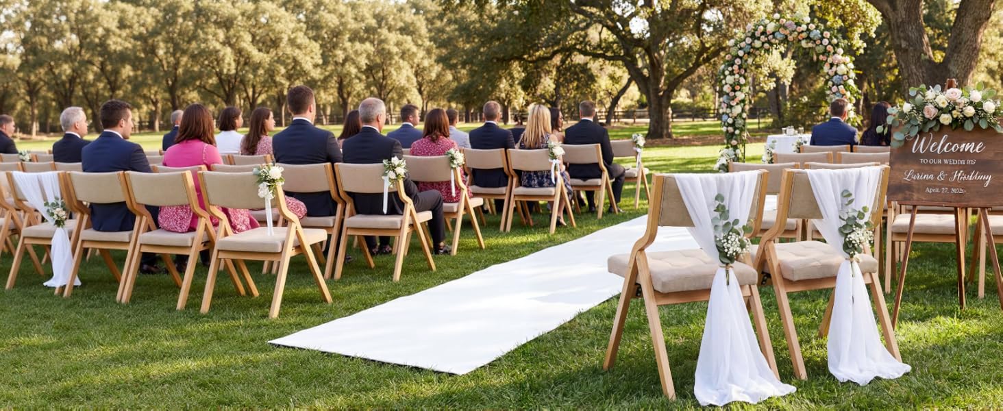 Outdoor event setup showing rows of white wooden chairs on grass, with decorative white fabric elements and floral arrangements for a ceremony setting.