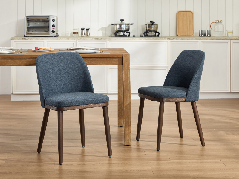 Serie de sillas decorativas modernas tapizadas en gris azulado con patas de madera oscura, que se muestran en diferentes ángulos contra los pisos de madera en un espacio interior luminoso.