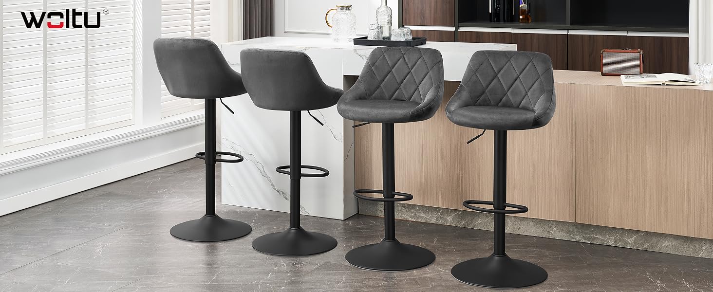 Four gray upholstered bar stools with quilted backs, adjustable height, and circular black bases. Positioned at a kitchen counter with wood cabinets visible in the background.