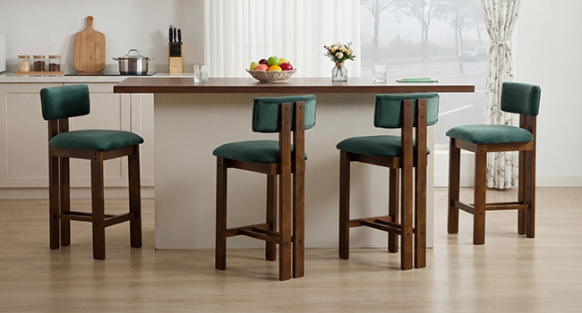 Moderna sala da pranzo con tavolo alto da bar in legno scuro e quattro sgabelli da bar imbottiti verde smeraldo. Tende bianche e decorazioni minimali da cucina visibili sullo sfondo.