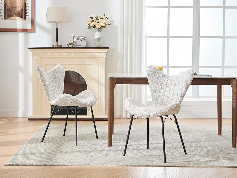 Dos sillas de comedor tapizadas en blanco con respaldos capitonados y patas de metal negro colocadas cerca de la repisa decorativa de una chimenea sobre una alfombra de color claro.