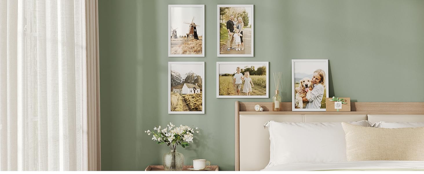 Soggiorno con pareti verde salvia con composizioni d'arte incorniciate, tende bianche ed elementi floreali decorativi.