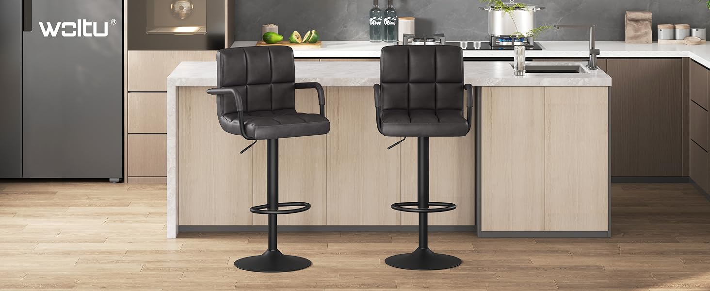 Modern kitchen island with two black adjustable bar stools, featuring light wood cabinets and a grey refrigerator in the background.