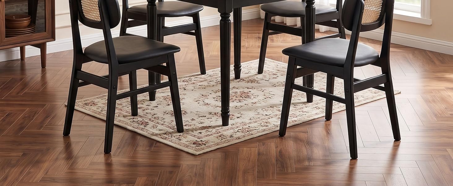 Table à manger en bois noir avec chaises noires assorties à dossiers incurvés, positionnées sur un tapis de couleur claire dans un espace intérieur recouvert de parquet.