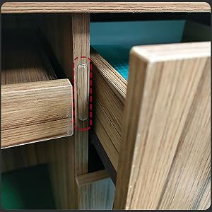 Close-up of wooden furniture joints, showing a red metal clip connecting two wooden panels. Smooth light-colored wood grain visible on all surfaces.