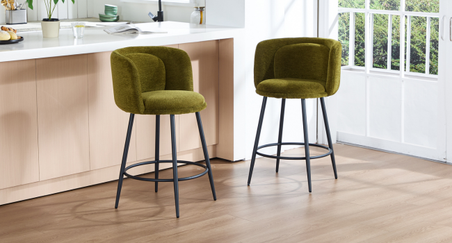 Moderne Barhocker mit samtähnlicher Polsterung in Olivgrün, positioniert in einem hellen Innenraum mit Holzboden.