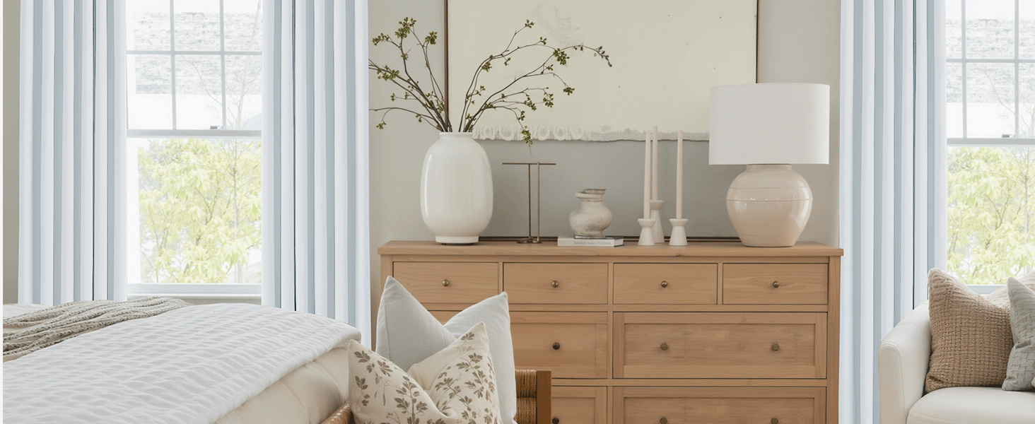 Luminosa sala de estar con cómoda de madera natural, cortinas blancas y jarrones decorativos. Grandes ventanales que proporcionan luz natural.
