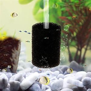 Cylindrical black aquarium filter sponge in operation, surrounded by white gravel and bubbles in clear water with green background.