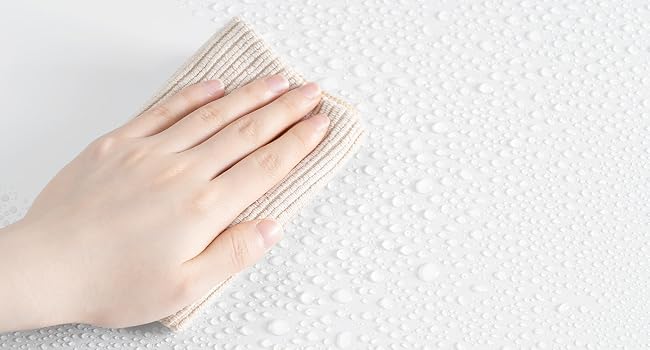 Limpiar a mano una superficie blanca texturizada con un paño beige. La superficie parece tener un patrón de hoyuelos o puntos, lo que sugiere que puede tratarse de una escena de limpieza o