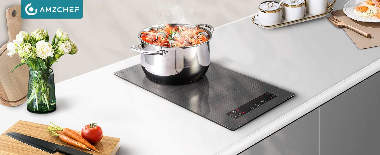 intégrée à un plan de travail de cuisine blanc. Casserole en acier inoxydable avec couvercle sur la surface de cuisson. A proximité : fleurs, légumes et ustensiles de cuisine.