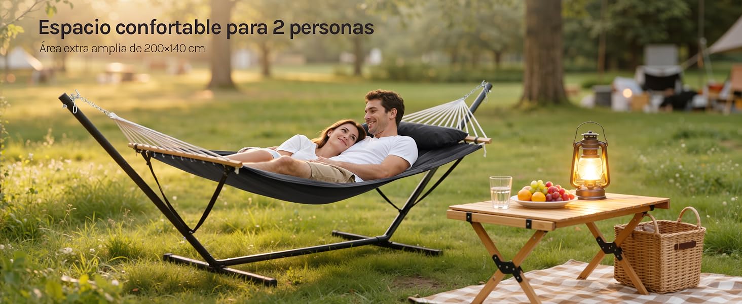 El texto dice «Espacio confortable para 2 personas». Escena exterior que muestra la disposición de una hamaca en un jardín soleado con accesorios de pícnic y una linterna.
