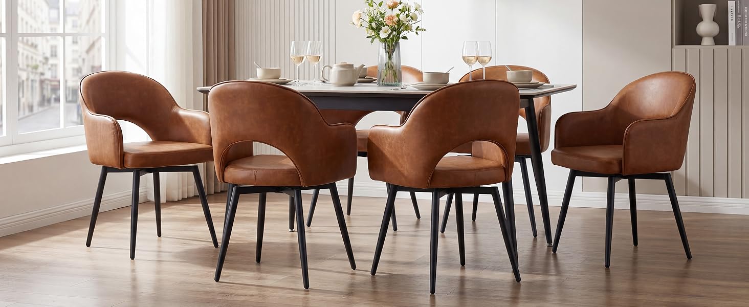 Set da pranzo con tavolo rettangolare in legno con quattro sedie imbottite color cognac con gambe in metallo nero disposte in uno spazio interno luminoso con finestre e decorazioni per la casa.