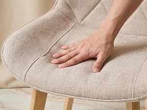 Pouf ou tabouret rond rembourré beige touchant la main, présentant une texture de tissu douce et une surface rembourrée.