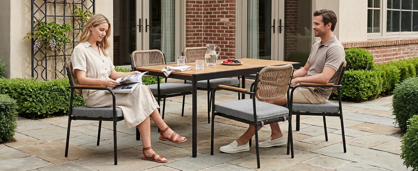 Scène de patio extérieur montrant deux personnes assises à une table à manger avec des chaises dans un jardin paysager avec des plantes et un bâtiment en brique en toile de fond.