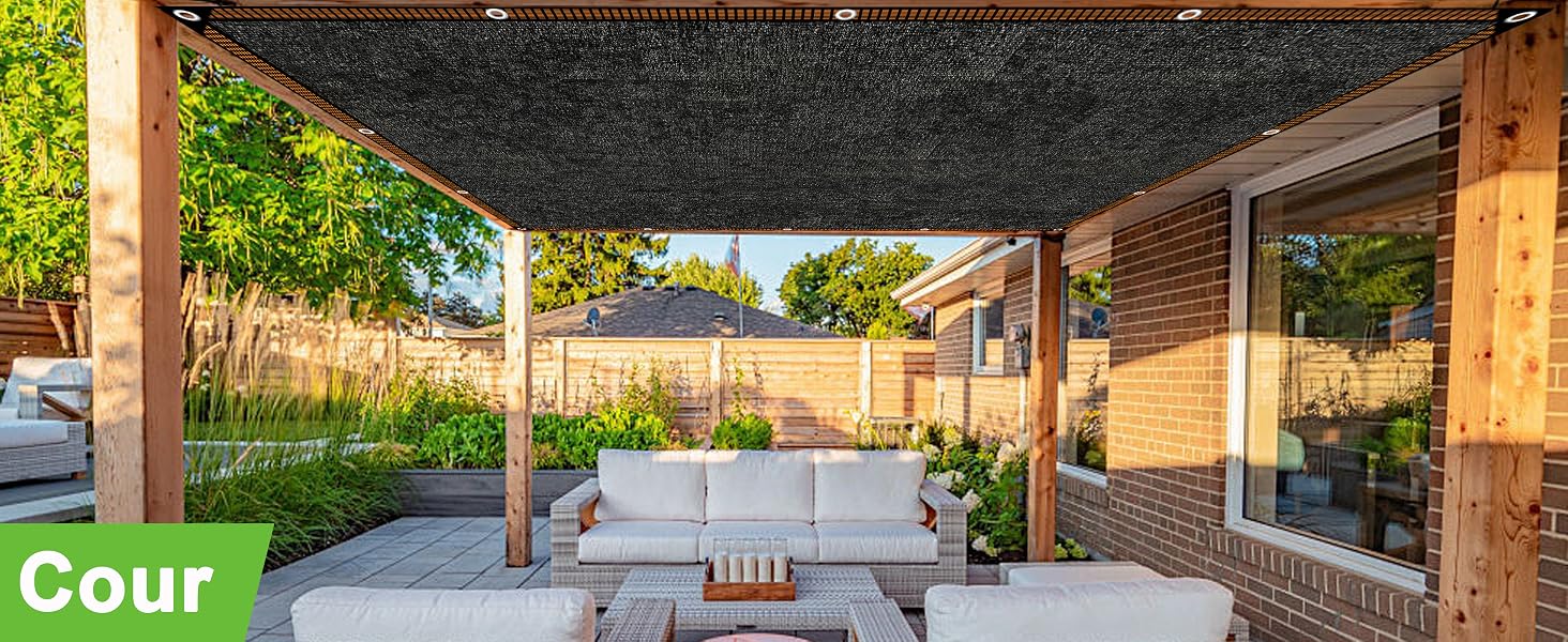 Espace extérieur couvert avec parasol noir, mobilier blanc et poteaux en bois, entouré d'une cour paysagée.